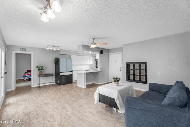 living room with a textured ceiling, light wood finished floors, baseboards, and ceiling fan