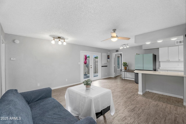 living area featuring light wood finished floors, rail lighting, visible vents, a ceiling fan, and a textured ceiling
