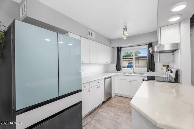 kitchen with range with electric cooktop, under cabinet range hood, stainless steel dishwasher, freestanding refrigerator, and white cabinetry
