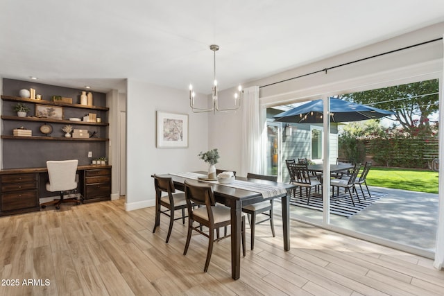 dining space with a notable chandelier, baseboards, built in desk, and light wood finished floors