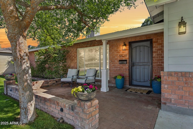 doorway to property featuring a porch and brick siding