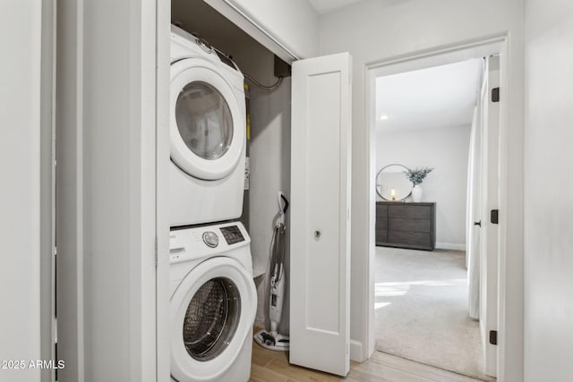 clothes washing area with light wood-style floors, baseboards, stacked washer and dryer, and laundry area