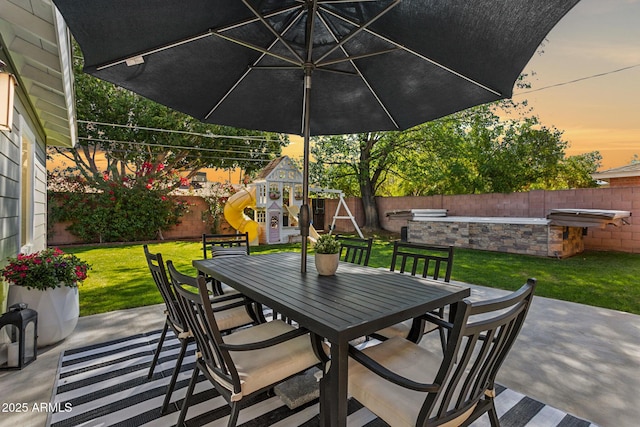 view of patio / terrace featuring outdoor dining space, a playground, and a fenced backyard