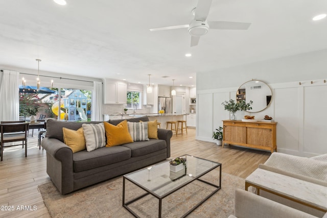 living area with a decorative wall, recessed lighting, ceiling fan with notable chandelier, and light wood-style floors