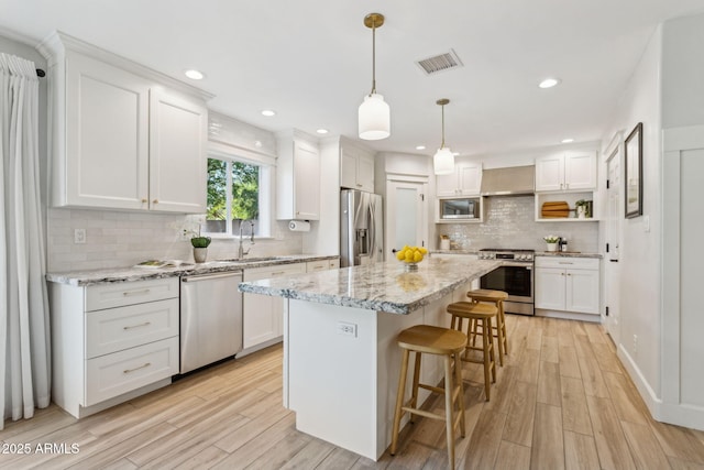 kitchen with a breakfast bar, a sink, stainless steel appliances, wall chimney exhaust hood, and white cabinets