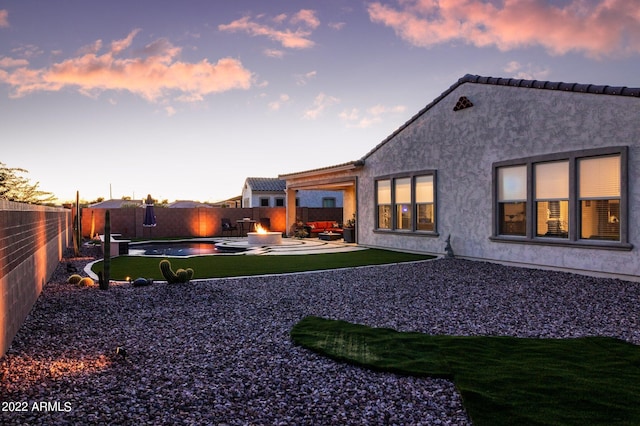 back house at dusk featuring a fenced in pool and a patio