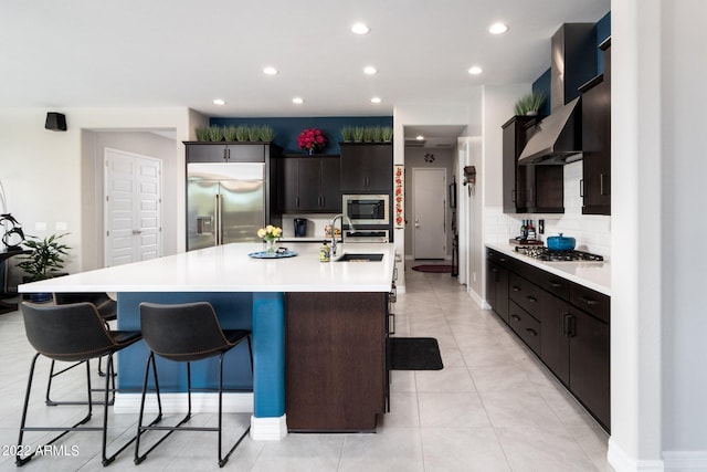 kitchen with sink, a kitchen breakfast bar, built in appliances, an island with sink, and decorative backsplash