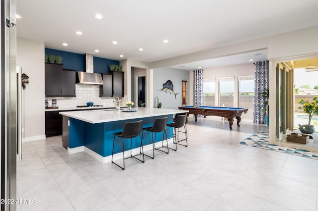 kitchen featuring sink, wall chimney range hood, a breakfast bar area, an island with sink, and decorative backsplash