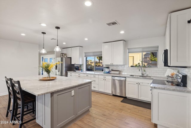 kitchen with appliances with stainless steel finishes, a kitchen island, decorative light fixtures, white cabinetry, and sink