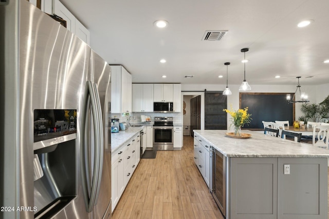 kitchen with white cabinets, a center island, stainless steel appliances, hanging light fixtures, and a barn door