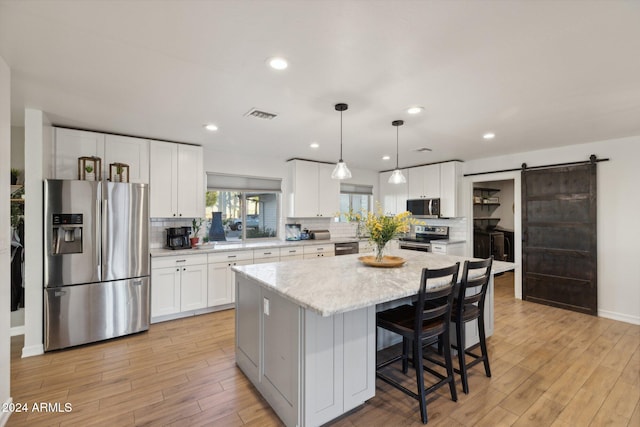 kitchen featuring white cabinets, appliances with stainless steel finishes, a center island, decorative light fixtures, and a barn door