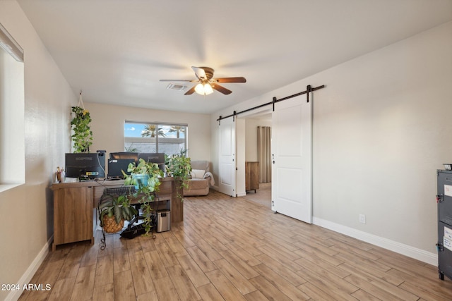 office area featuring light wood-type flooring, ceiling fan, and a barn door