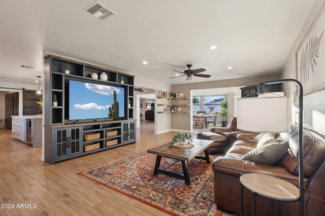 living room with ceiling fan, a barn door, and light wood-type flooring