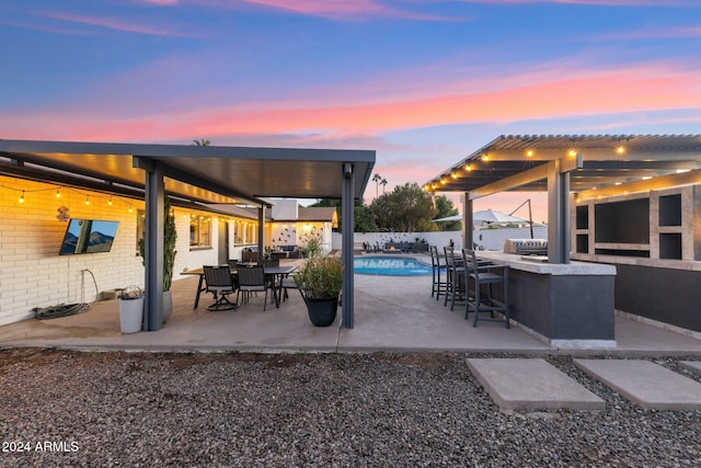 patio terrace at dusk with a fenced in pool and a bar