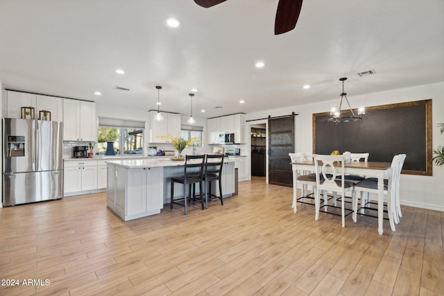 kitchen featuring stainless steel appliances, a barn door, white cabinets, and decorative light fixtures