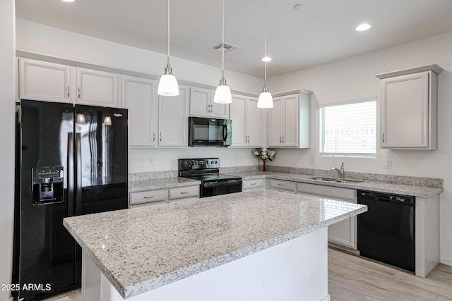 kitchen with pendant lighting, a center island, black appliances, sink, and light stone counters