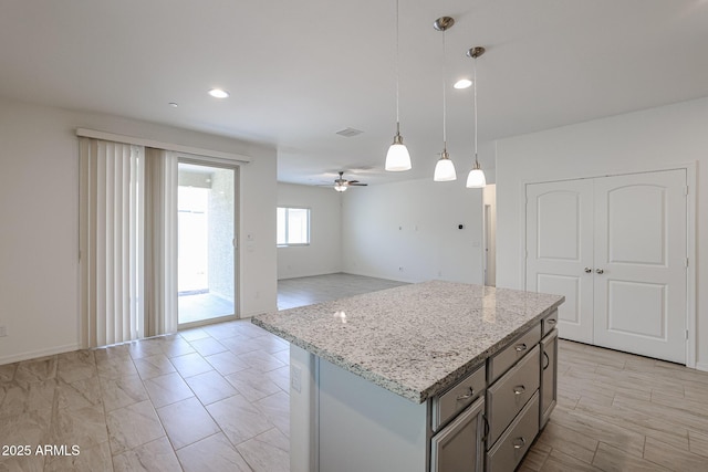 kitchen with light stone countertops, ceiling fan, a center island, and pendant lighting