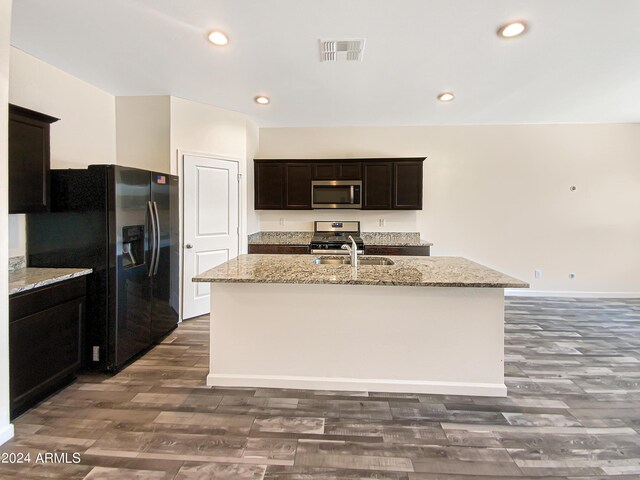 kitchen with wood-type flooring, range, black fridge, light stone counters, and a center island with sink