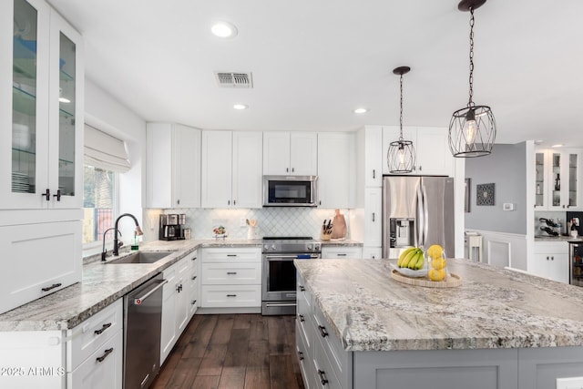 kitchen with a sink, visible vents, appliances with stainless steel finishes, a center island, and glass insert cabinets