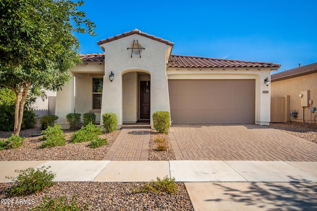 mediterranean / spanish house featuring a tiled roof, decorative driveway, an attached garage, and stucco siding