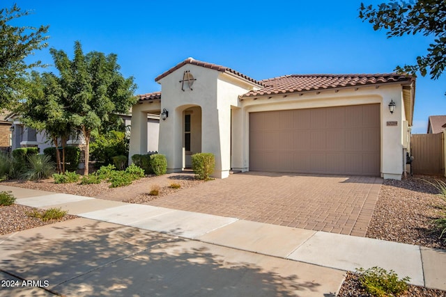 mediterranean / spanish house with a tiled roof, decorative driveway, an attached garage, and stucco siding