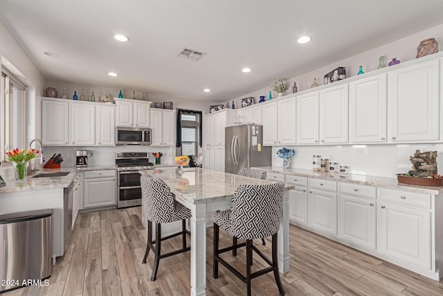 kitchen featuring white cabinets, a kitchen island, appliances with stainless steel finishes, light hardwood / wood-style floors, and light stone counters