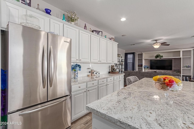 kitchen with stainless steel refrigerator, white cabinetry, light stone countertops, tasteful backsplash, and light hardwood / wood-style flooring