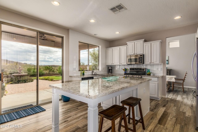 kitchen with white cabinetry, light stone counters, backsplash, a kitchen island, and appliances with stainless steel finishes