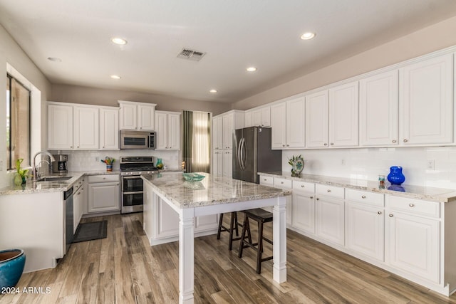 kitchen featuring appliances with stainless steel finishes, sink, hardwood / wood-style flooring, a center island, and white cabinetry