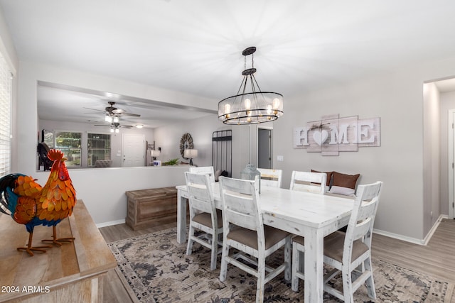 dining area with ceiling fan with notable chandelier and light hardwood / wood-style flooring