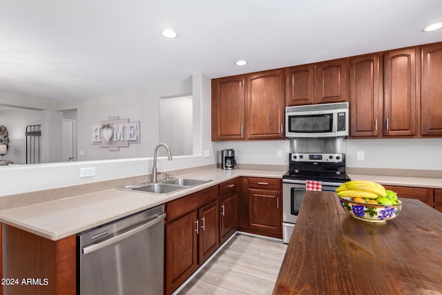 kitchen featuring appliances with stainless steel finishes, sink, kitchen peninsula, and light hardwood / wood-style flooring