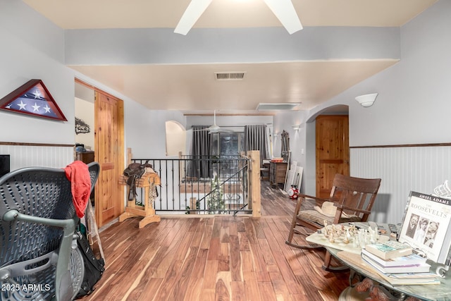 interior space with arched walkways, wood finished floors, an upstairs landing, visible vents, and wainscoting