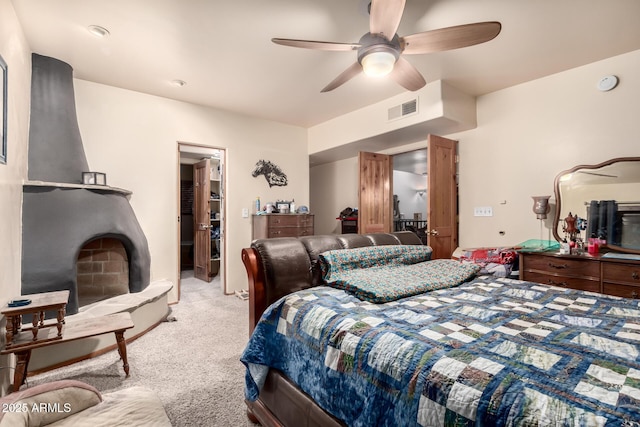 carpeted bedroom featuring visible vents, a walk in closet, and a ceiling fan