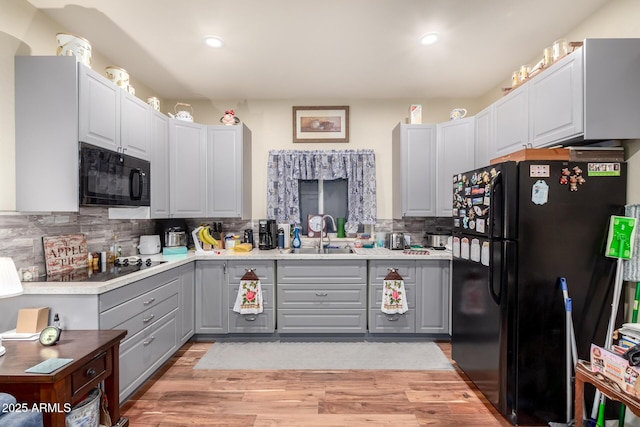 kitchen featuring black appliances, light wood-style flooring, a sink, and gray cabinetry