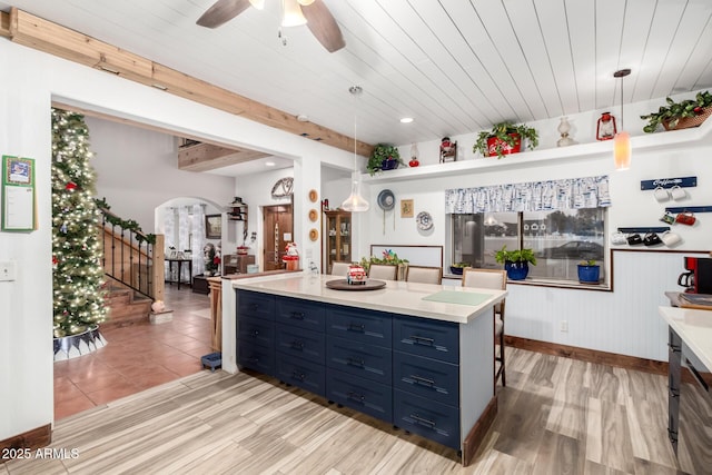 kitchen with arched walkways, blue cabinets, hanging light fixtures, light countertops, and light wood-type flooring