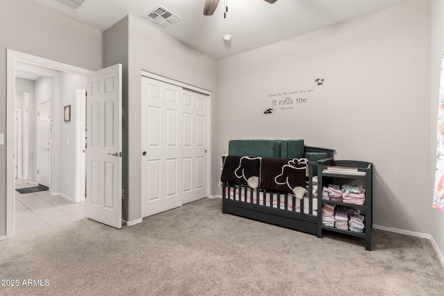 bedroom featuring a crib, light colored carpet, ceiling fan, and a closet