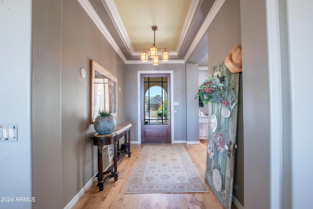 entrance foyer featuring crown molding, light hardwood / wood-style flooring, a chandelier, and a raised ceiling