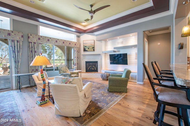 living room with light hardwood / wood-style floors, crown molding, a tray ceiling, and a fireplace