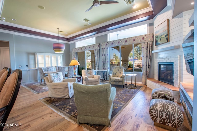 living room with crown molding, light hardwood / wood-style flooring, a fireplace, and a raised ceiling