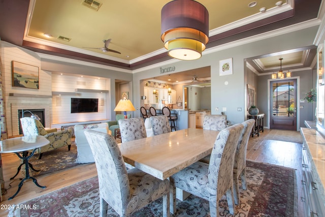 dining area with a raised ceiling, ornamental molding, light hardwood / wood-style flooring, and a brick fireplace