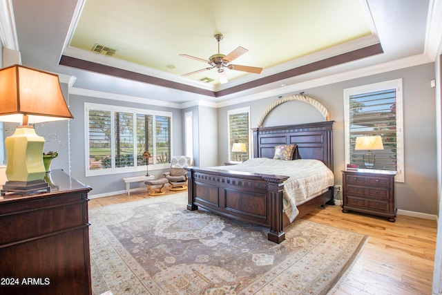 bedroom with ornamental molding, ceiling fan, light wood-type flooring, and a raised ceiling