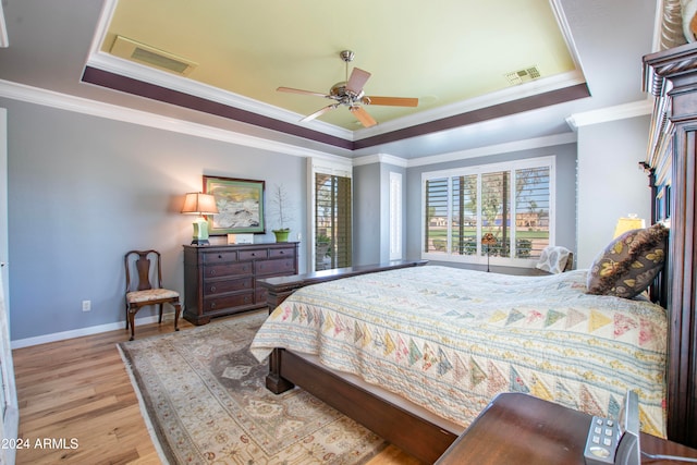 bedroom featuring ceiling fan, a tray ceiling, light hardwood / wood-style flooring, and crown molding