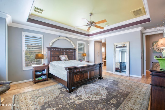 bedroom with light hardwood / wood-style flooring, ornamental molding, a tray ceiling, and ceiling fan