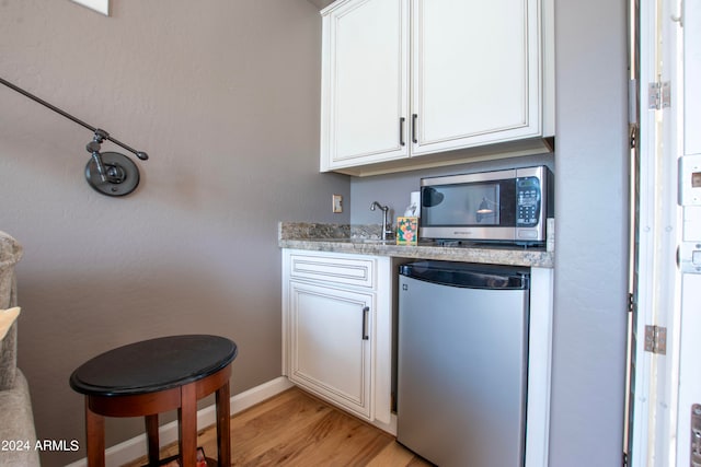 kitchen with light stone countertops, white cabinets, light hardwood / wood-style flooring, and stainless steel appliances