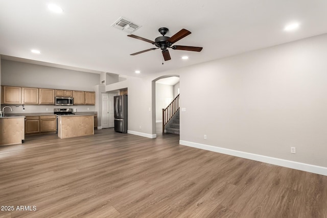 unfurnished living room featuring a sink, visible vents, baseboards, stairs, and light wood-type flooring