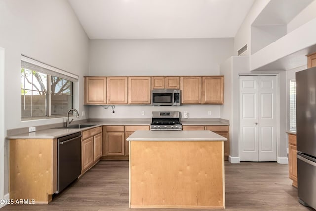 kitchen featuring light countertops, appliances with stainless steel finishes, light brown cabinets, a sink, and a kitchen island