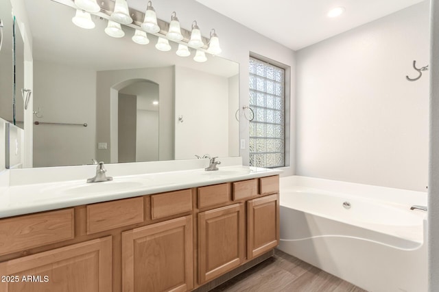 bathroom with wood finished floors, a garden tub, a sink, and double vanity