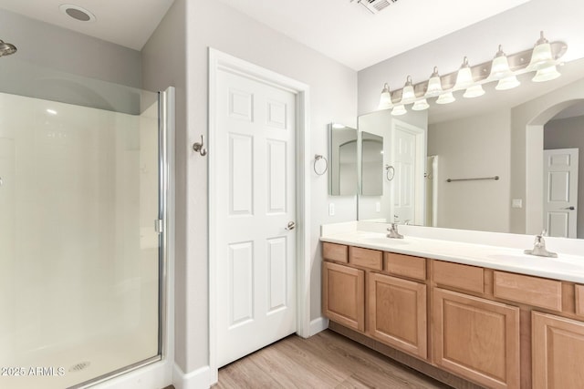 bathroom with a stall shower, double vanity, a sink, and wood finished floors