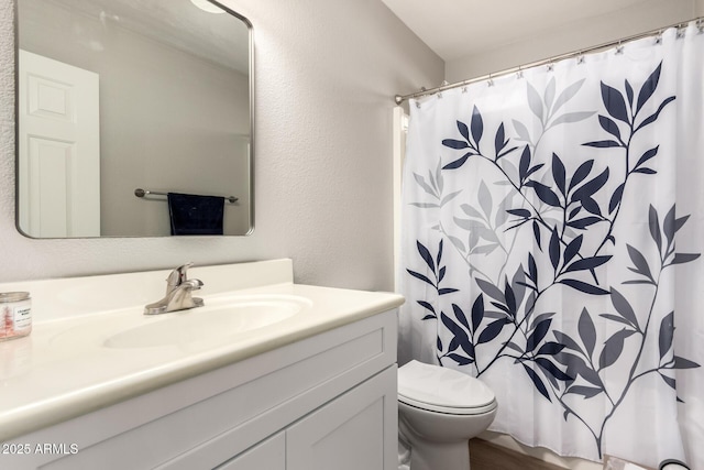 bathroom with a textured wall, curtained shower, vanity, and toilet