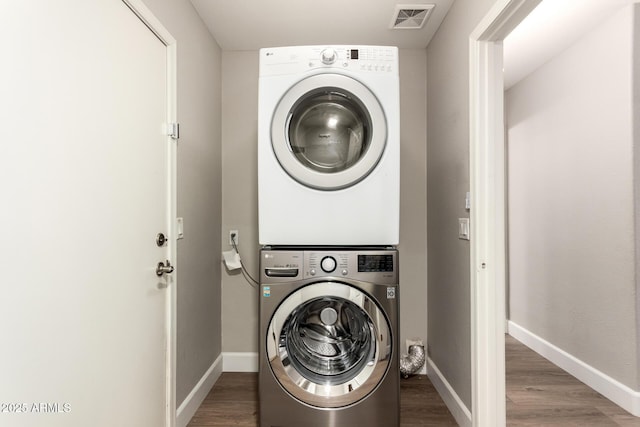 laundry room with laundry area, stacked washing maching and dryer, wood finished floors, and visible vents